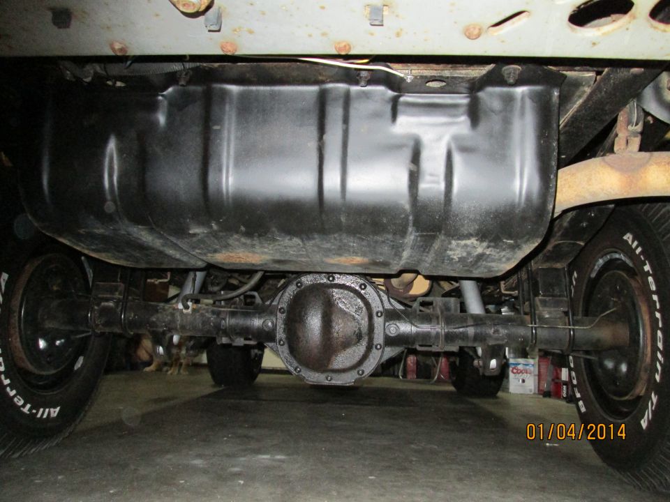 Underside of a vehicle showing a large black fuel tank and rear axle with All-Terrain tires