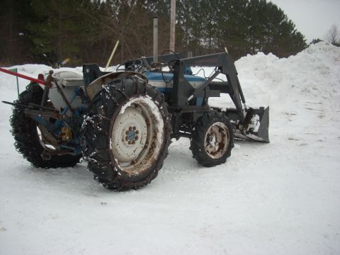 1963 Hummer H3 - A blue tractor equipped with a front loader and snow chains is parked in a snowy environment.
