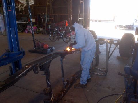 1985 Jeep CJ7 - A person is welding a vehicle frame in a workshop, with a car lift and bicycles visible in the background.