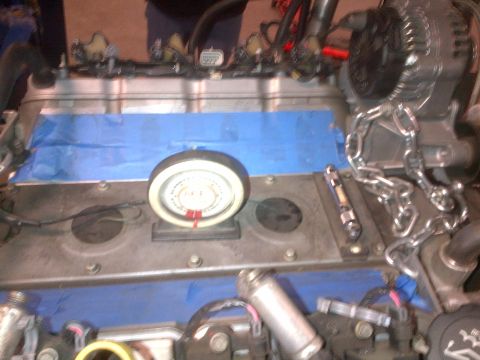 1985 Jeep CJ7 - Close-up of an engine part with a gauge and chain, likely during a repair or build.