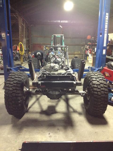 1985 Jeep CJ7 - The chassis and engine of a Jeep CJ are suspended on a lift, indicating a custom build or restoration project in progress.