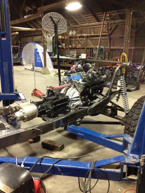 1985 Jeep CJ7 - The chassis of a Jeep is shown in a workshop, with the engine and transmission mounted.