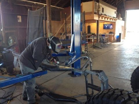 1985 Jeep CJ7 - A person welds a vehicle frame in a workshop, with a unique loft living space visible in the background.