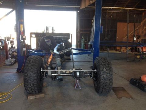 1985 Jeep CJ7 - Frame of a Jeep CJ being modified in a workshop with a lift and tools.