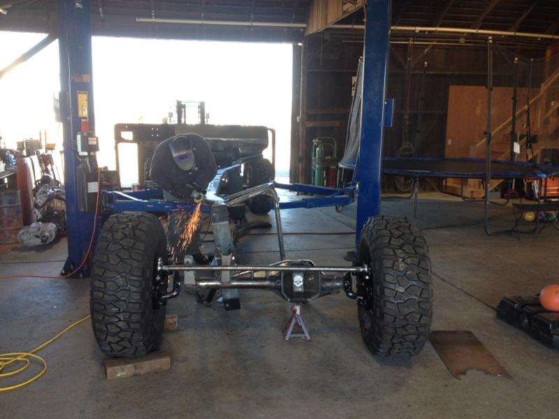 Jeep CJ frame with large tires, being worked on by a person with a grinder