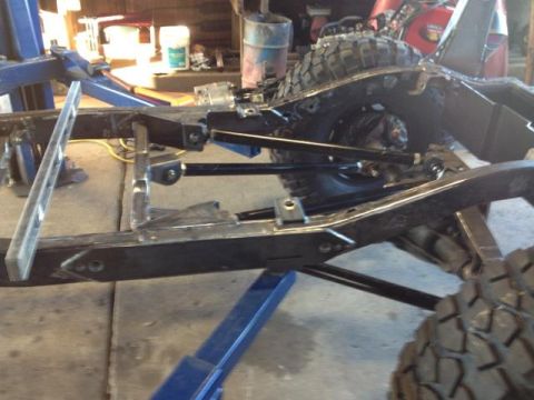 1985 Jeep CJ7 - The frame of a Jeep CJ is being worked on in a garage, with a lift and tools present.