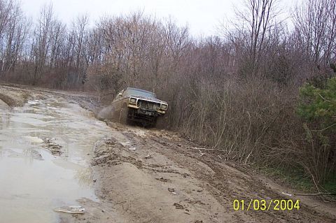 1978 Ford Bronco - A 1978 Ford Bronco navigates a muddy off-road trail with trees in the background.
