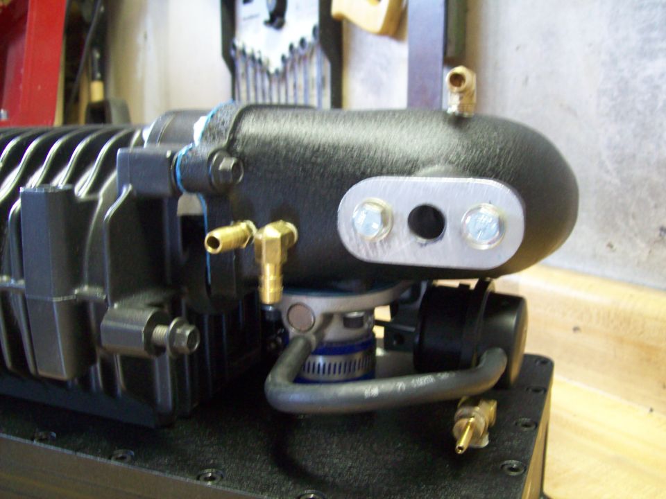Black supercharger with brass fittings and a metal plate with two holes