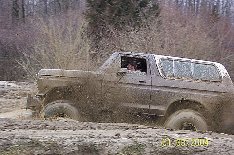 1978 Ford Bronco - A 1978 Ford Bronco navigates a challenging muddy off-road course, kicking up significant spray.