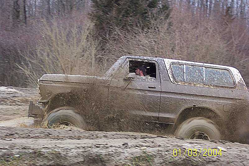 Mud-splattered 1978 Ford Bronco driving through a muddy terrain
