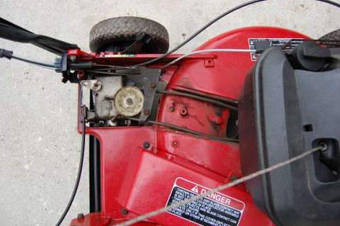 2006 Honda RANCHER - Close-up view of a red lawnmower's engine and deck, showing mechanical components and a safety warning label.
