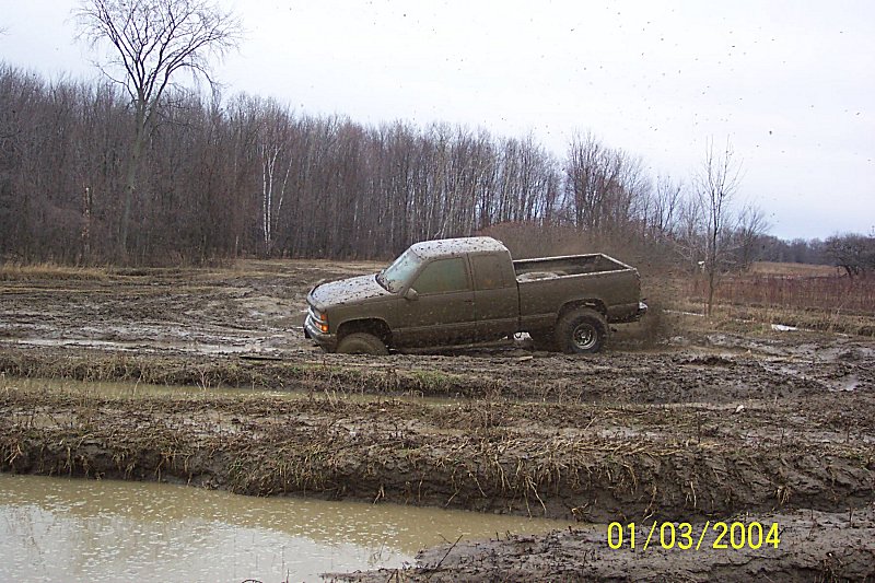 Pickup truck stuck in a muddy field with trees in the background