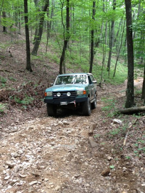 1989 Ford Bronco - Teal Ford Bronco navigating a rough, wooded path.
