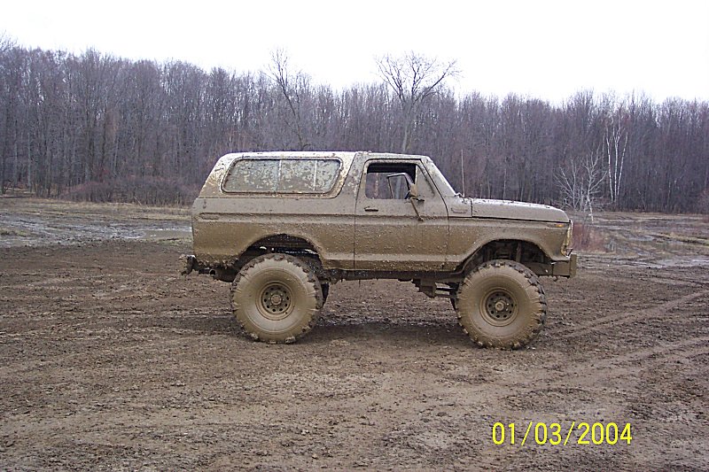 Mud-covered 1978 Ford Bronco parked on a muddy field with trees in the background