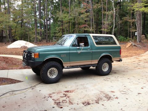1989 Ford Bronco - This lifted Ford Bronco is shown from the side, with a wooded area and construction in the background.