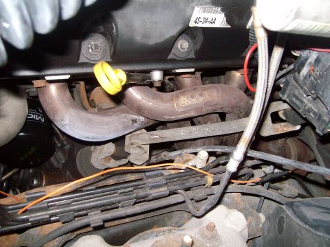 2004 Ford Crown Victoria - Engine compartment detail showing exhaust manifold and associated components, with visible part numbers and wiring.
