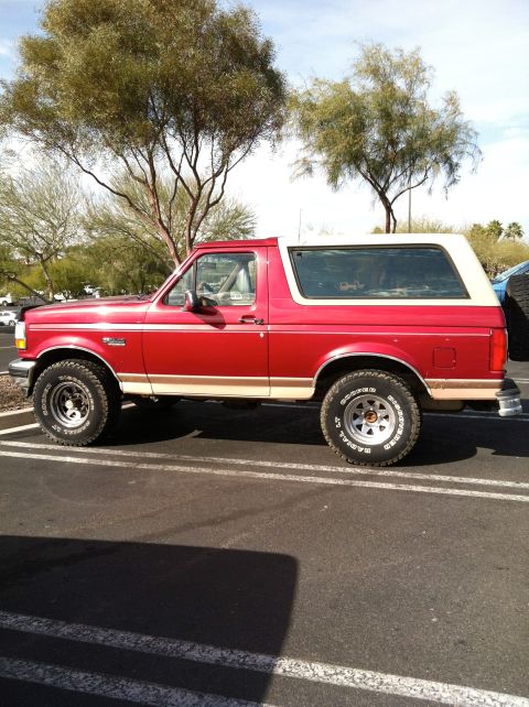 1994 Ford Bronco - This red and white 1994 Ford Bronco is parked in a lot, showing its side profile.