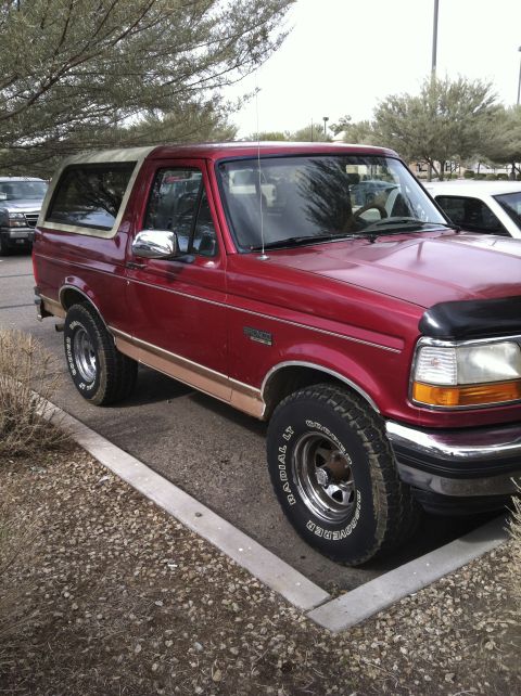 1994 Ford Bronco - Red 1994 Ford Bronco parked in a lot with trees and other vehicles nearby.