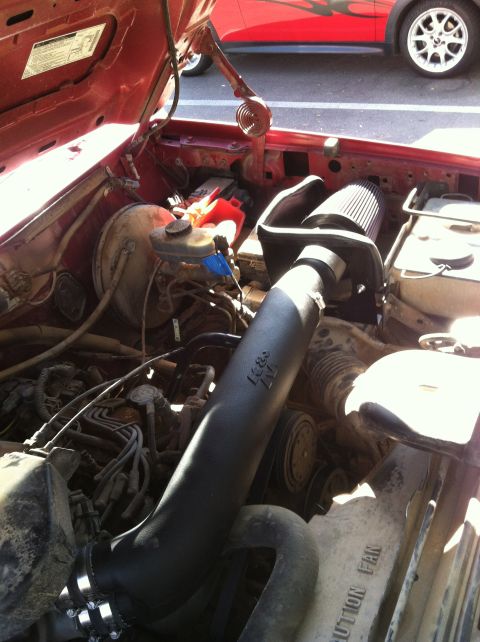 1994 Ford Bronco - Engine bay of a red vehicle, an aftermarket K&N air intake system. Another red vehicle is visible in the background.