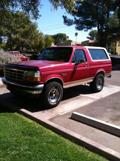 1994 Ford Bronco - Red 1994 Ford Bronco with a tan stripe and white roof parked outside.