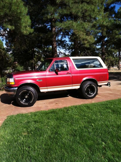 1994 Ford Bronco - Side view of a red and white 1994 Ford Bronco with a white removable top.