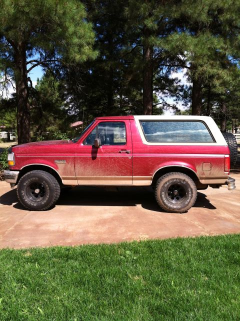 1994 Ford Bronco - Side view of a red and white Ford Bronco with a spare tire mounted on the rear.