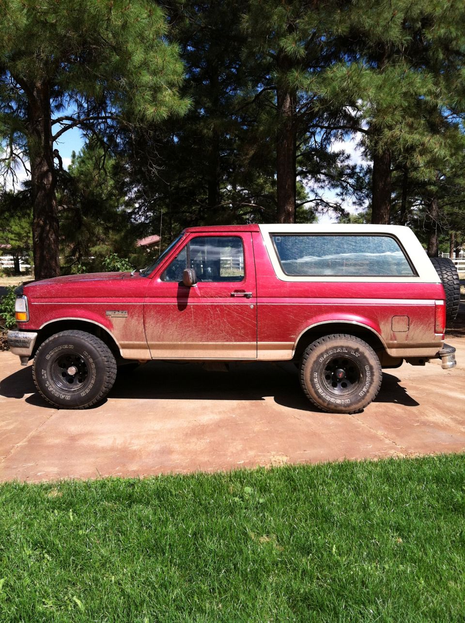 Red and white Ford Bronco parked on a concrete driveway, covered in dirt