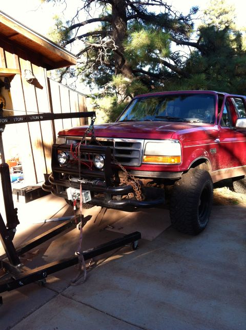 1994 Ford Bronco - Red 1994 Ford Bronco is parked outside a building with a cherry picker positioned over its front end.