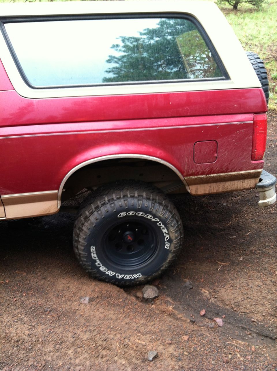 Red 1992 Ford Bronco rear quarter panel, tan trim, and tire on dirt road. Spare tire mounted on rear door