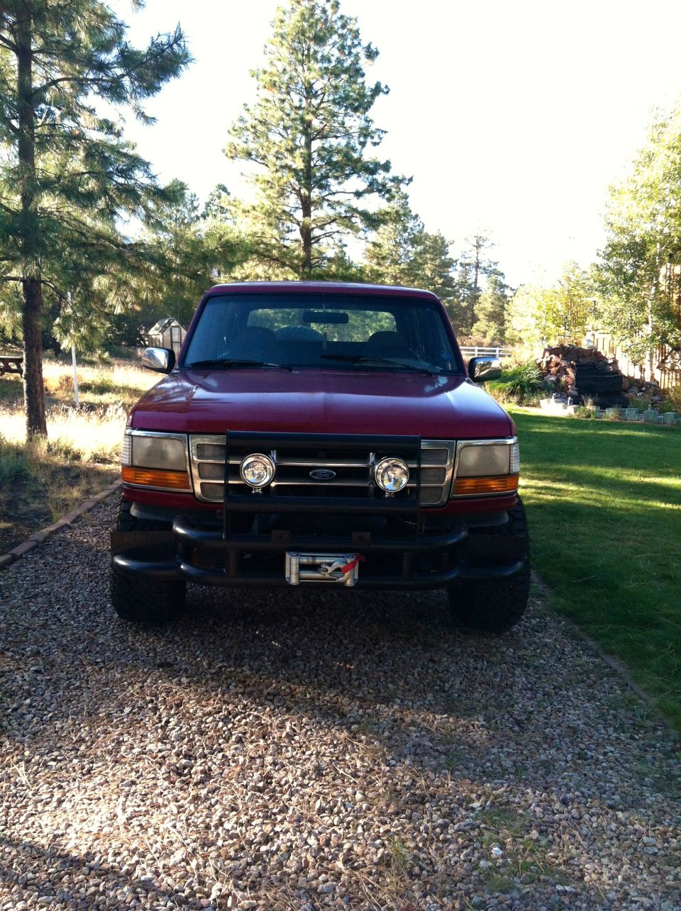 Red Ford Bronco with black bull bar and auxiliary lights, parked on gravel