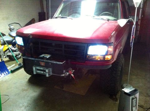 1994 Ford Bronco - This red Ford Bronco is parked indoors with its headlights on, showing a custom winch bumper.