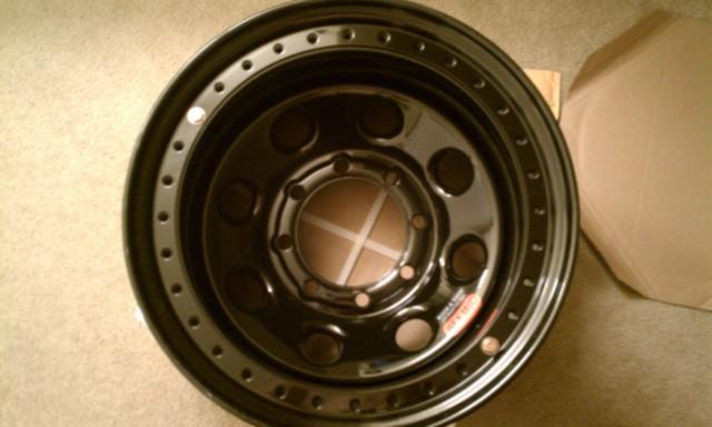 black alloy wheel with multiple bolt holes and a red sticker