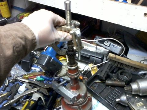 1998 Ford Crown Victoria - A mechanic uses a specialized tool to remove a part from a distributor assembly on a workbench.