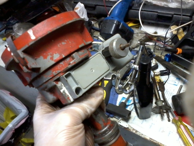 Hand holding a red and gray automotive distributor with tools in the background