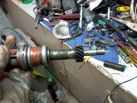 1998 Ford Crown Victoria - A distributor part is held in a gloved hand, with various tools scattered on a workbench in the background.