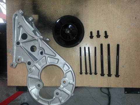 1994 Ford Bronco - Parts for a vehicle's engine, including an alternator bracket, pulley, and mounting bolts, are arranged on a workbench.