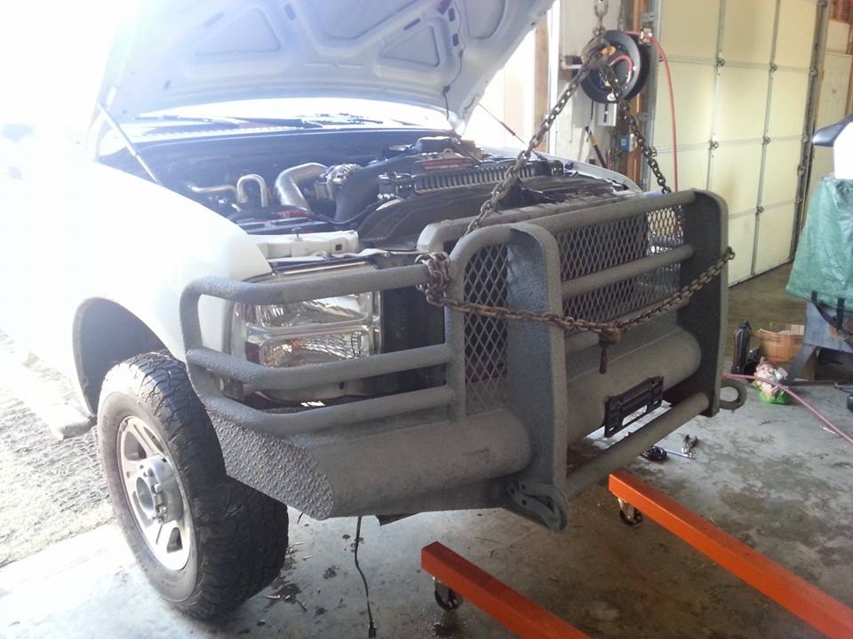 Truck front end with hood open, engine exposed. A large aftermarket grille guard is attached. The truck is on an engine hoist