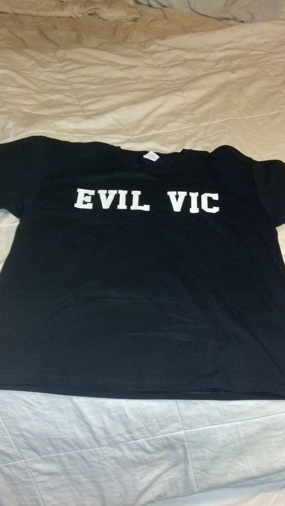 Black t-shirt on a bed printed with the white text EVIL VIC