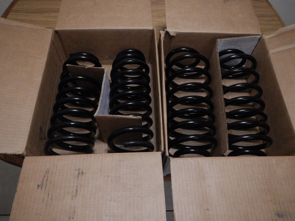 Two open cardboard boxes holding four black coil springs