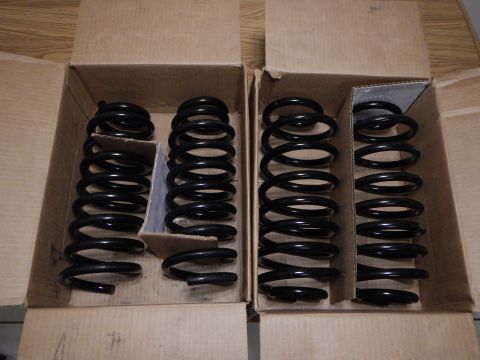2003 Ford Crown Victoria - Two pairs of black coil springs are arranged in open cardboard boxes on a wooden surface.