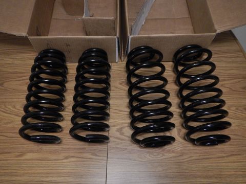 2003 Ford Crown Victoria - Four black coil springs of two different lengths stood upright on a wood-grain surface in front of open boxes.