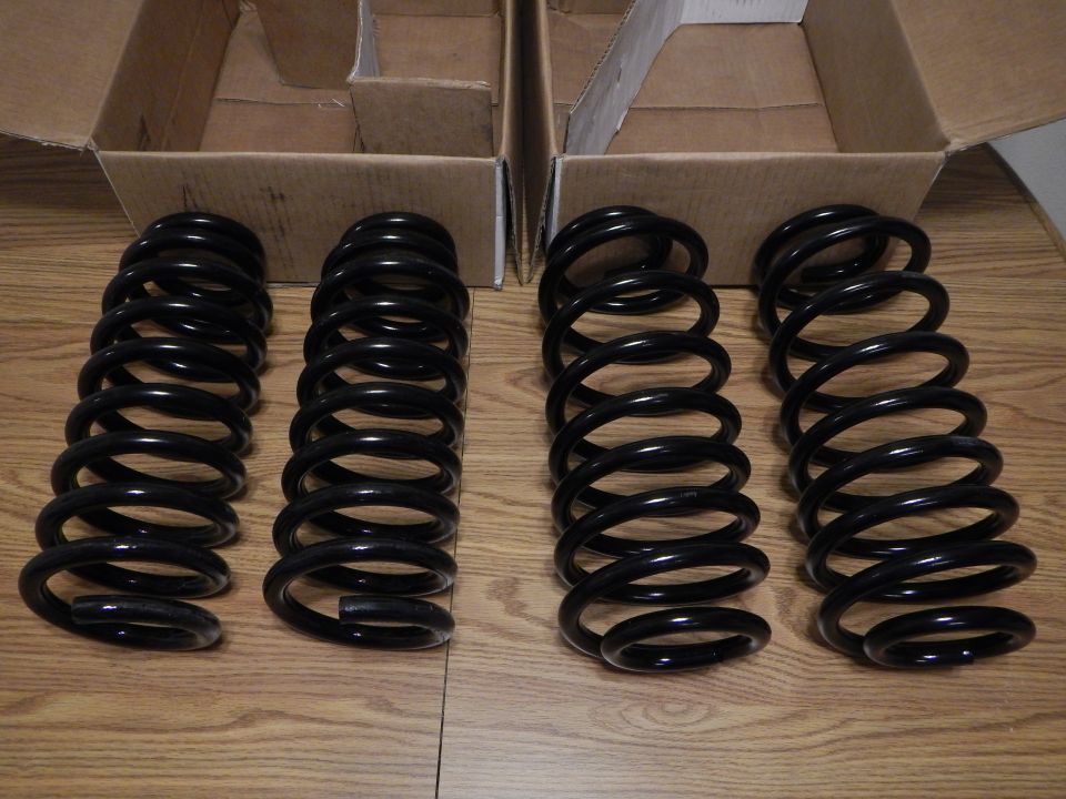 Four black coil springs standing on a wood table near open boxes