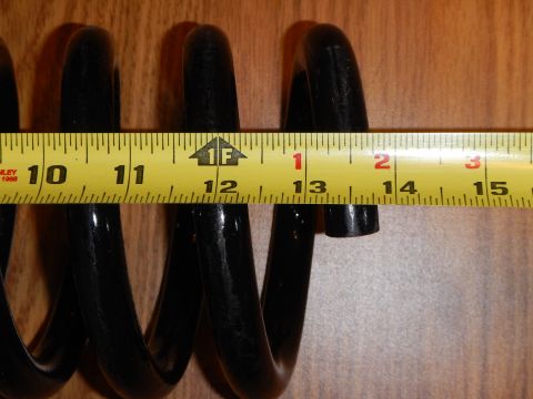 2003 Ford Crown Victoria - black coil spring measured against a yellow tape measure on wood, near the 12 inch mark.