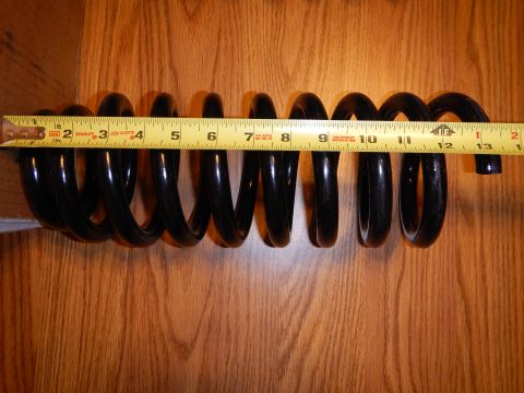 2003 Ford Crown Victoria - black coil spring laid horizontally on a wood-grain surface next to an extended yellow tape measure.