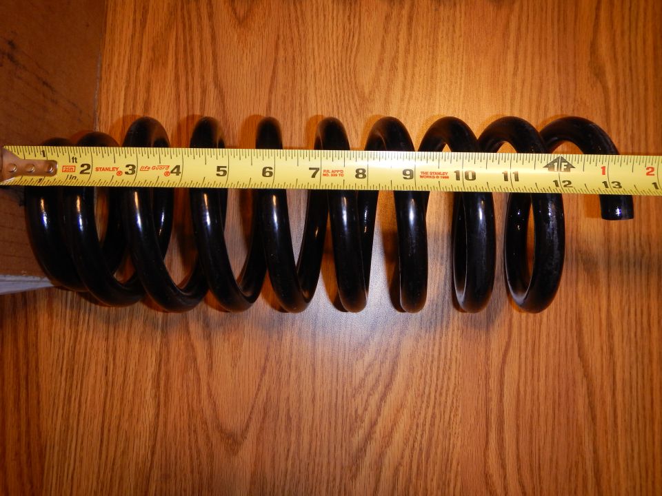 Black coil spring laid beside a tape measure on a wood surface