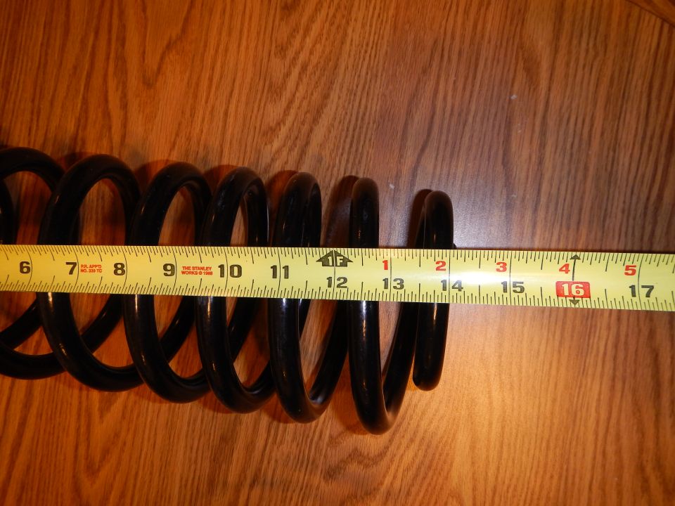 Black coil spring laid beside a tape measure on a wood-grain table