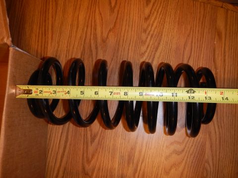 2003 Ford Crown Victoria - long black coil spring laid horizontally on wood beside a tape measure, with a cardboard box at the edge.