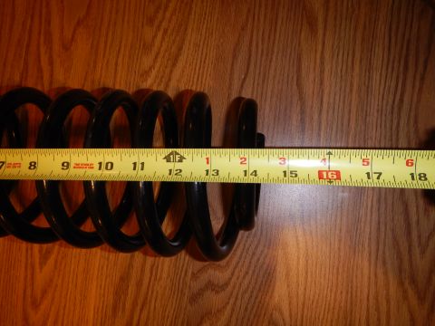 2003 Ford Crown Victoria - black coil spring laid on a wood-grain surface alongside a yellow tape measure for length reference.