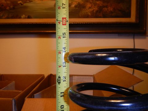 2003 Ford Crown Victoria - dark blue-black coil spring stood upright beside a vertical tape measure, with a framed painting on the wall behind.