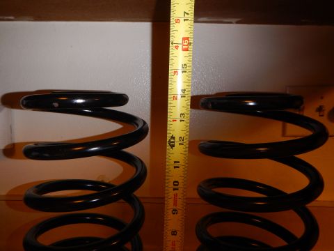 2003 Ford Crown Victoria - Two black coil springs stood upright on a shelf beside a vertical tape measure against a light wall.